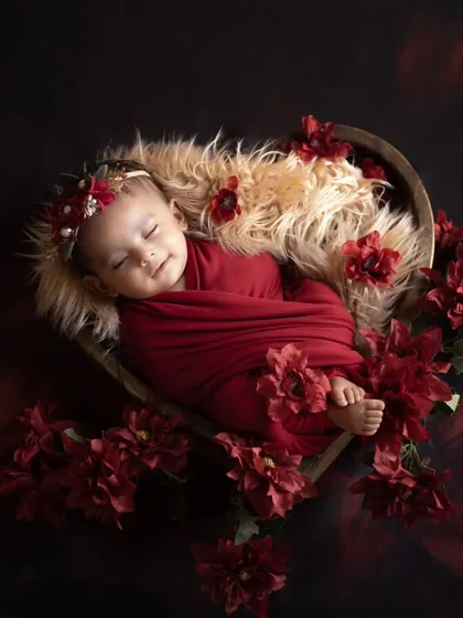 A heart full of love. This newborn is nestled in a heart-shaped bowl, surrounded by rich red flowers, symbolizing the love they've brought into the world.