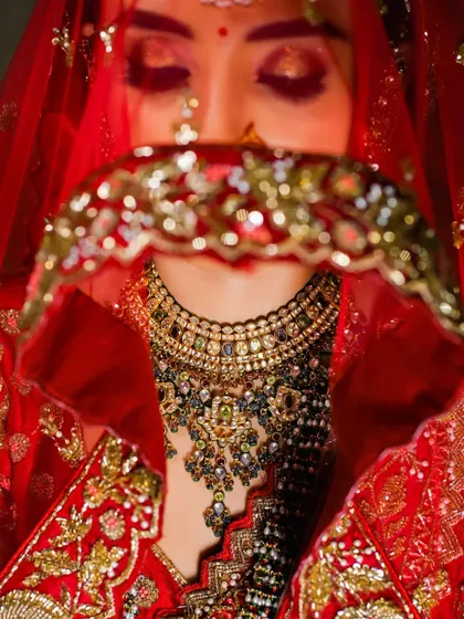 An artistic close-up of the bride, her face partially obscured by her red veil. This shot focuses on her stunning statement necklace and creates a sense of traditional mystery.