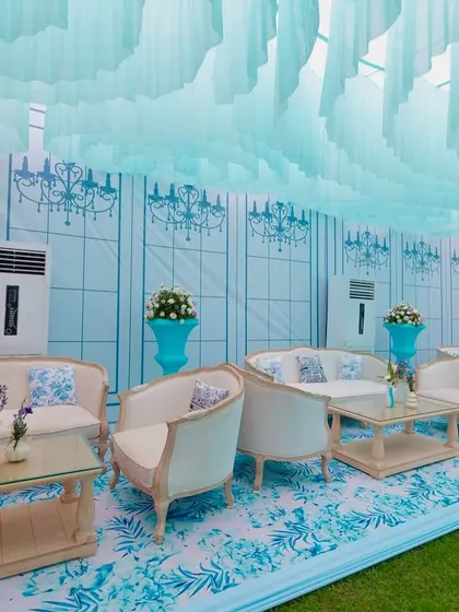 A luxurious lounge area at the Dior-themed Mehendi, featuring plush white sofas, custom-printed cushions, and a backdrop wall with elegant chandelier motifs.