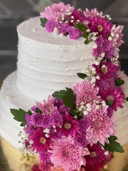 A two-tiered white cake decorated with a cascading arrangement of fresh purple and pink flowers. This design is perfect for weddings, offering a touch of natural beauty and elegance.