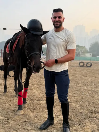 A full-length shot of a rider and his horse, showcasing the proper equestrian gear, from boots to helmet.