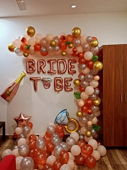 A fun and stylish "Bride to Be" decoration. This home setup features a rose gold and silver balloon arch, foil letters, and champagne and ring-shaped foil balloons.