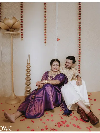 A relaxed and intimate portrait of a couple sitting amidst flower petals in a beautifully decorated indoor setting.