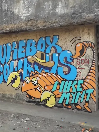A slightly different angle of the "Jukebox Cowboys" mural, showing more of the surrounding weathered wall and metal gate, which gives context to its urban location in Virar.