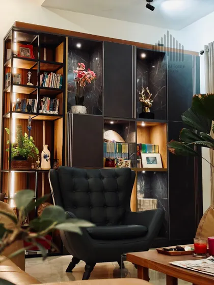 A close-up of a sophisticated living room corner, featuring a dark-toned display unit with marble-finish back panels and accent lighting. The tufted armchair adds a classic touch to this modern space.