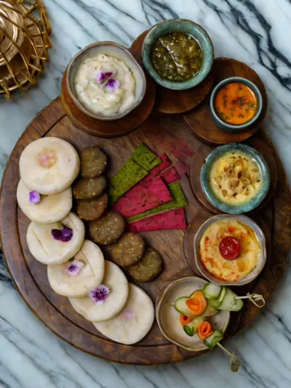 An overhead shot of a beautifully arranged Lebanese platter on a wooden board. It showcases a variety of dips, falafel, mini pitas, and colorful vegetable chips, garnished with edible flowers for an elegant touch. This is perfect for a small, sophisticated gathering.