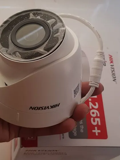 Holding a new Hikvision dome camera, showing the protective film still on the lens.