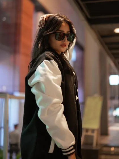 A profile shot of a model in a varsity jacket. The blurred background and her confident pose create a classic and cool street fashion image.