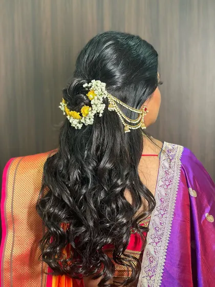 A Maharashtrian bridal look with a half-updo, adorned with fresh yellow flowers and a traditional ear chain. It's a beautiful blend of modern and traditional styles.