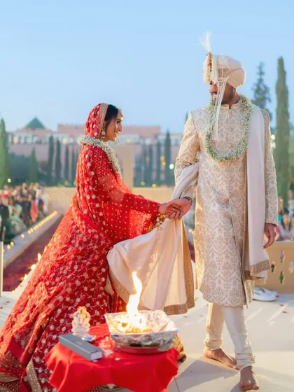 The couple performing the wedding rituals during their Hindu ceremony in Marrakech. The setting, with the Atlas Mountains in the distance, adds a layer of natural beauty to the sacred moment.