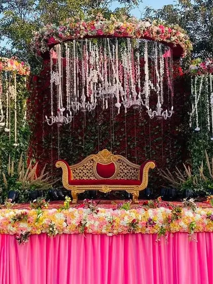 A lush and romantic stage design, with a backdrop of greenery and hanging chandeliers, all framed by a cascade of flowers.