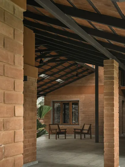 A covered walkway supported by brick pillars provides a sheltered path between different parts of the home. It frames a view of a quiet seating area, creating a sense of discovery as one moves through the space.
