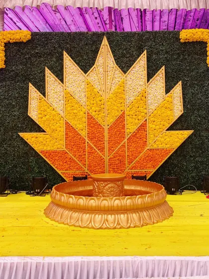 This geometric lotus backdrop for a Haldi ceremony was crafted using petals of yellow and orange marigolds. The design combines modern patterns with the traditional flower of celebration, all centered around a brass urli.