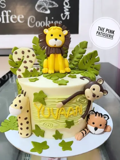 A jungle-themed cake for a second birthday. This design features a lion, giraffe, tiger, and monkey surrounding the cake, with a wood grain texture on the name.