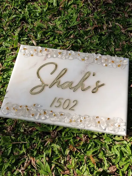 This marble effect nameplate is a great example of simple elegance. It features a clean white marble design with the family name in golden mirror acrylic, bordered by natural stones and gold-plated chips for a touch of sparkle.