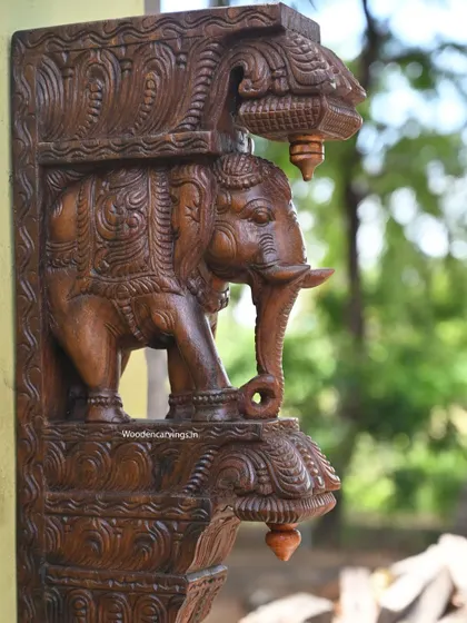 A close-up of the elephant bracket, focusing on the detailed carving of the head and trunk. The wax brown finish gives the wood a warm, natural luster.