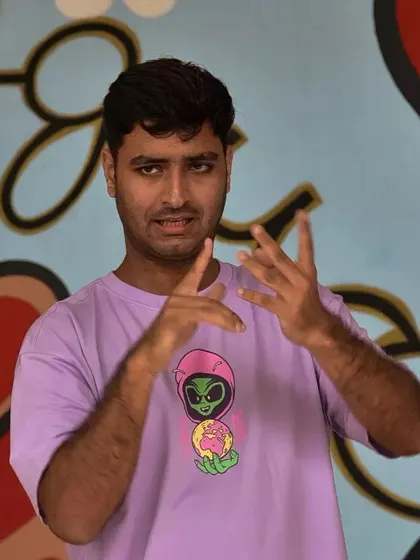 A Deaf instructor passionately explaining a concept in Indian Sign Language against a colorful mural. Our workshops are dynamic, visual, and engaging.