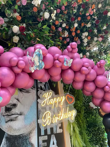 A close-up of the 50th birthday decor, showing the "Happy Birthday" neon sign against a custom art backdrop, framed by a vibrant pink balloon arch.