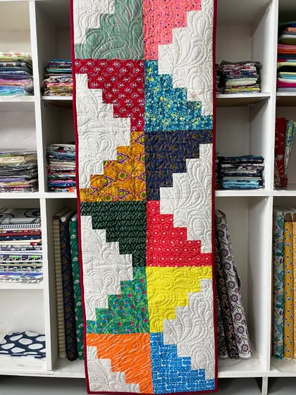 A colorful "log cabin" style table runner or wall hanging, with each block made of contrasting light and dark fabric strips.