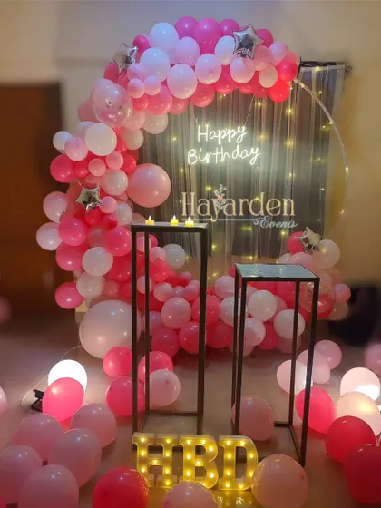 A romantic half-ring balloon setup in shades of pink. The fairy light curtain and scattered balloons on the floor create a dreamy atmosphere.