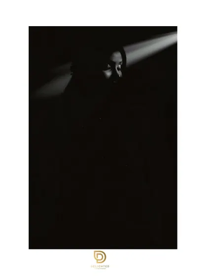 A highly artistic and minimalist bridal portrait. The single beam of light in the darkness creates a mysterious and dramatic effect, focusing all attention on her face.