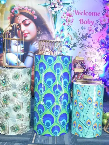 A closer look at the Krishna-themed decor, showing the custom-printed pedestals with peacock feather designs. A small Krishna idol is placed inside a decorative birdcage.