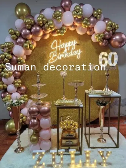 A lavish 60th birthday setup with a gold glitter backdrop, a rose gold and white balloon arch, and a full dessert table display.