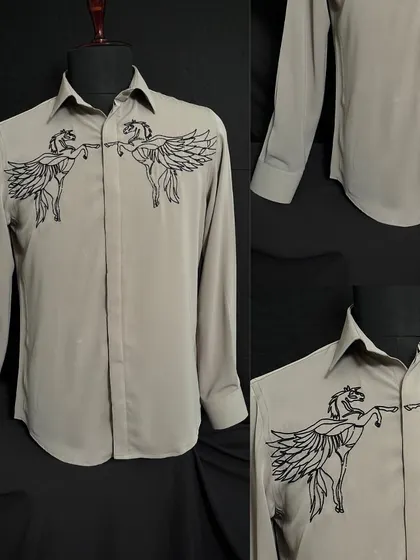 A detailed look at the beige shirt with two winged horses meeting at the chest. The black embroidery creates a stark, graphic effect on the neutral-toned fabric.