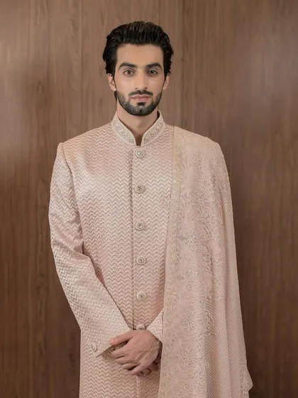 A full-length portrait displaying the impeccable tailoring of our rose gold sherwani. The clean lines and sophisticated embroidery make it a standout choice for a groom or wedding guest.