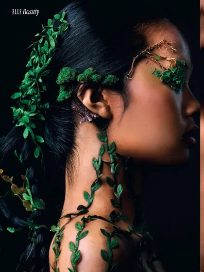 A profile view showcasing the seamless integration of green vines into the model's hair and across her body. The dramatic side lighting against a black background emphasizes the organic textures and sculptural quality of the styling.