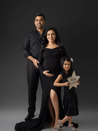 The big sister announcement. The family poses together, and their daughter proudly holds a star-shaped sign that says "Big Sister," making her an important part of the maternity photoshoot.