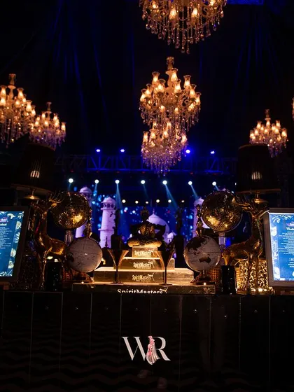 The cocktail bar is ready for party time. Custom neon signs, digital menus, and an array of spirits are set under the glow of chandeliers, making the bar a central hub of energy and style.