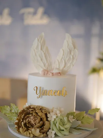 A close-up of a beautiful custom cake for a baptism. The delicate angel wings and floral details show the artistry that goes into our dessert offerings.