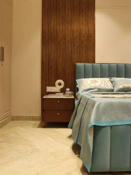 This master bedroom design blends classic elegance with contemporary comfort, featuring a pastel blue upholstered bed and a rich wooden fluted panel.
