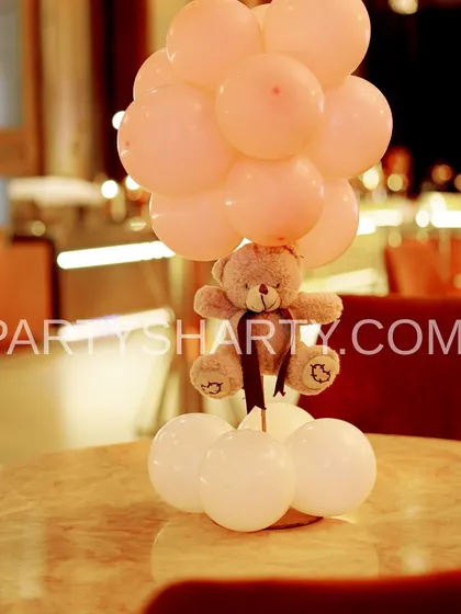 A simple yet charming teddy bear centerpiece, where a small teddy is lifted by a bunch of pink balloons.