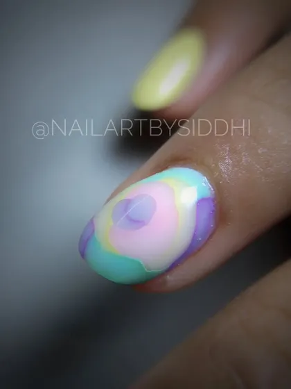 A close-up of a single nail with a "blooming gel" floral design, where colors spread to create a soft, layered flower effect.
