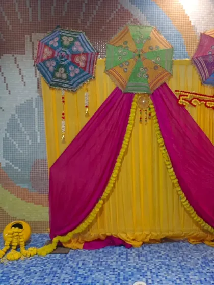 A poolside Haldi setup with a backdrop of yellow and pink drapes, decorated with Rajasthani umbrellas. The colorful mosaic tiles of the pool area complement the festive decor.
