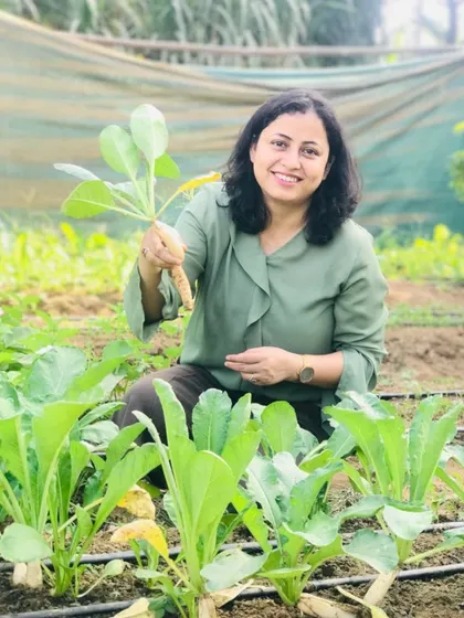 A visitor kneels in the field, happily holding up a knol kohl she has just harvested. The joy of connecting with the source of our food is evident.