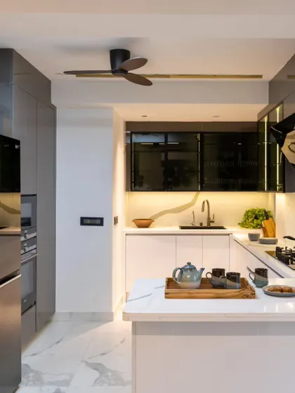 A modern, minimalist kitchen in a Jaipur penthouse. The pure white theme and marble-look flooring amplify the sense of space, while tinted glass and grey cabinets add drama and sophistication.