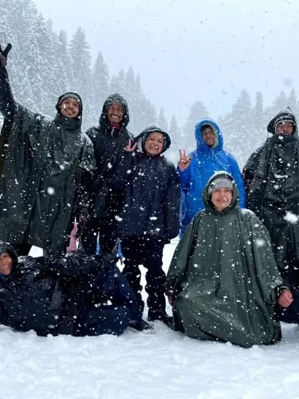 Our group of happy trekkers, clad in ponchos, enjoying a fresh snowfall at Juda Ka Talab campsite during the Kedarkantha trek. These are the moments of pure, unadulterated joy.
