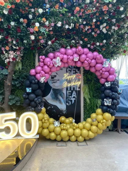 The full view of a unique and artistic 50th birthday setup, featuring a circular balloon frame in pink, black, and gold around a modern art piece.