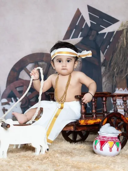 This little farmer is ready to work, sitting on a bullock cart in a traditional veshti.