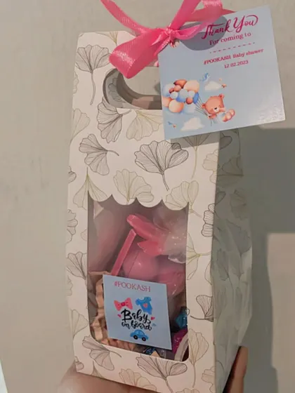 A close-up of our "Pookash" baby shower favor, featuring a custom tag and a mix of pink and blue items.