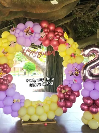 An outdoor butterfly theme for a 2nd birthday, with a circular balloon arch in pastel yellow, pink, and purple.