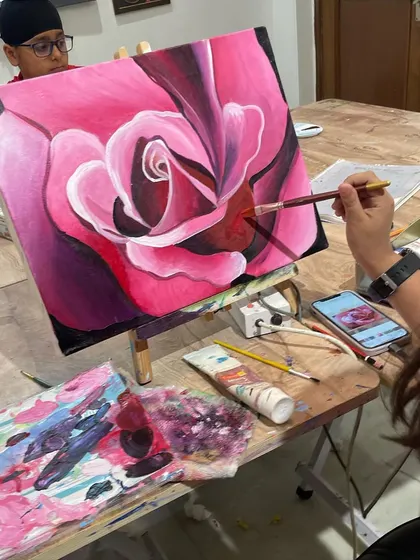 A close-up of a student painting a vibrant pink rose. We focus on layering colors to create the soft, velvety texture of the petals.