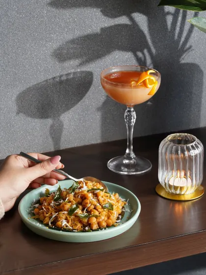 A moody, atmospheric shot of a chickpea dish and a cocktail, using shadows to create a sophisticated and intimate dining vibe.