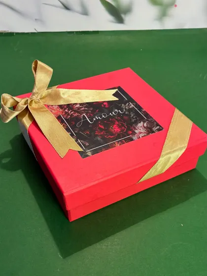 The elegant packaging for my Rakhi floral candle. The vibrant red box with a floral motif and gold ribbon makes it a beautiful and thoughtful gift for your brother and sister-in-law.