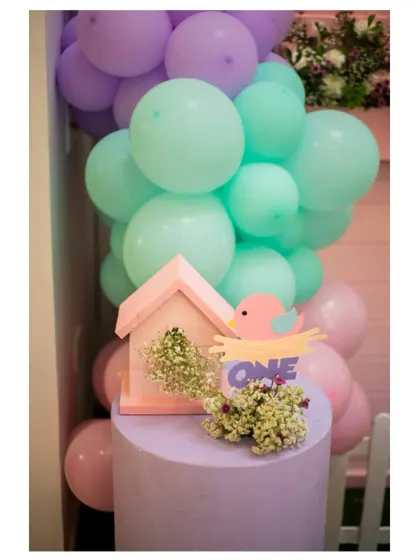 A close-up of a birdhouse prop and a 'ONE' sign, nestled in a pastel balloon garland.