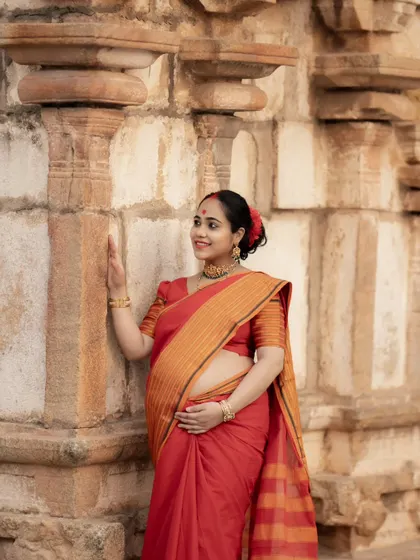 A solo portrait of the mother-to-be at a temple, gently touching the ancient stone walls. Her traditional attire and serene expression create a timeless image.