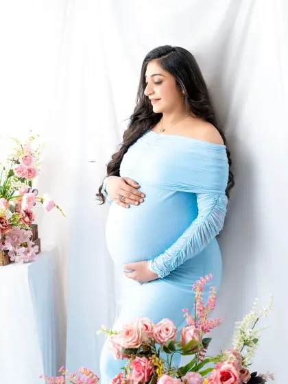 A serene portrait in powder blue. The mother-to-be is surrounded by soft pink flowers, creating a gentle and romantic color palette.